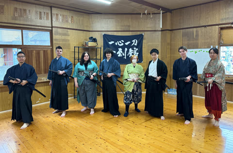 Person in black kimono handling a sword near a sword rack.