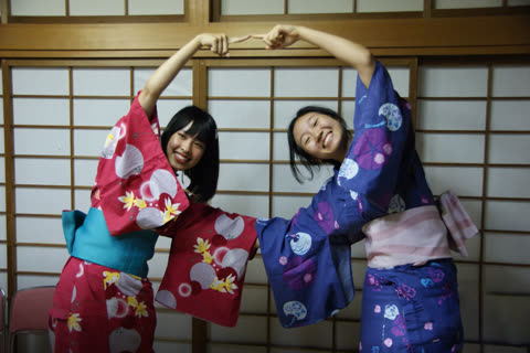 Two women in kimonos seated at a table, smiling.